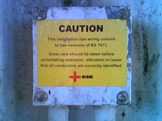 An electricity distribution board.  A label
reads “This installation has wiring colours to two versions of BS
7671.  Great care should be taken before undertaking extension, alteration
or repair that all conductors are correctly identified.”